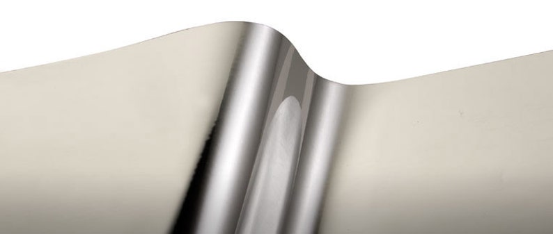 May include: A close-up of a silver metallic sheet with a slight bend. The sheet has a smooth, reflective surface.