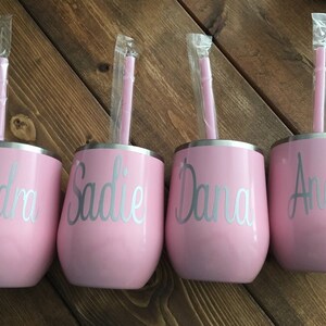 May include: Four pink stainless steel tumblers with silver straws and personalized names: Kendra, Sadie, Dana, and Andrea.
