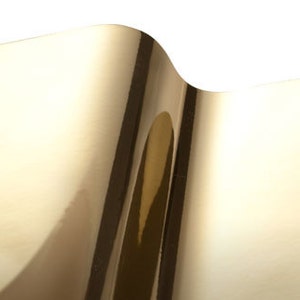 May include: A sheet of gold metallic vinyl with a reflective surface. The vinyl is folded over on itself, creating a wave-like effect.