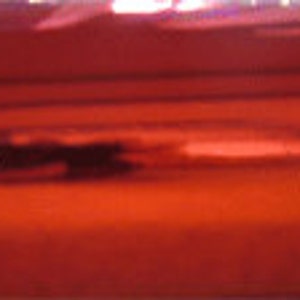 May include: A close-up of a red metallic surface with a slight sheen. The surface is smooth and reflective.
