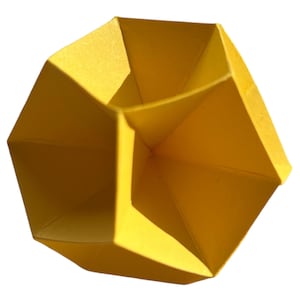 Op de afbeelding: Een gele geometrische origami-vorm met meerdere facetten.