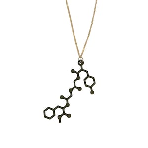 Puede incluir: Un collar de cadena dorada con un colgante con forma de estructura química. El colgante está hecho de metal verde oscuro.