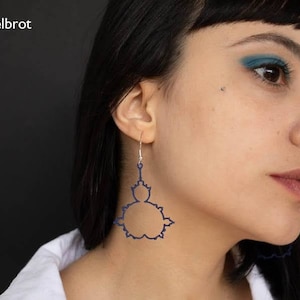 Puede incluir: Una persona lleva un par de pendientes con un diseño geométrico azul oscuro. Los pendientes tienen forma de flor estilizada.