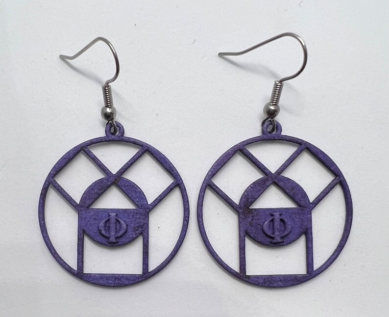 May include: A pair of purple earrings with a geometric design and a Greek letter Phi in the center. The earrings are made of metal and have a silver hook.