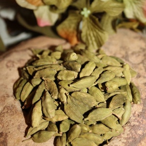May include: A close-up of a pile of green cardamom pods. The pods are arranged in a random pattern and are illuminated by a warm light.