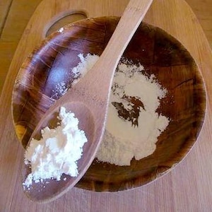 May include: A wooden spoon filled with white powder sits in a wooden bowl with more powder. The bowl and spoon are on a wooden surface.