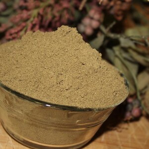 May include: A glass bowl filled with a mound of light brown powder. The powder is finely ground and has a uniform texture.