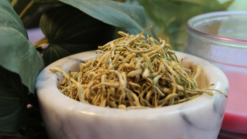 May include: A white marble mortar and pestle filled with dried, light brown flower buds.