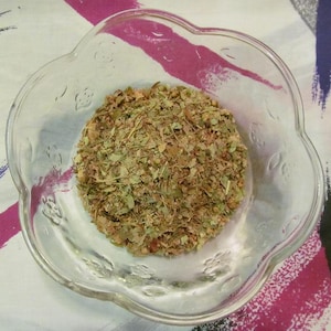 May include: A clear glass bowl filled with a mixture of dried herbs and leaves. The herbs are a mix of green, brown, and red.