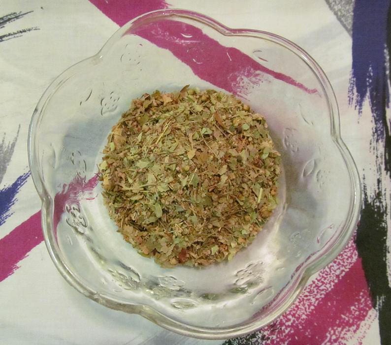 May include: A clear glass bowl filled with a mixture of dried herbs and leaves. The herbs are a mix of green, brown, and red.