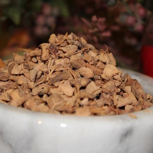 May include: A white marble mortar and pestle filled with dried, brown ginger root pieces.
