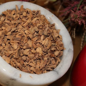 May include: A white marble mortar and pestle filled with dried, brown, chopped root bark.