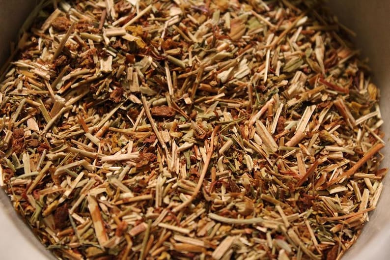 May include: Close-up of a bowl filled with dried herbs and flowers. The herbs are a mix of brown, tan, and green, with some yellow flowers mixed in.