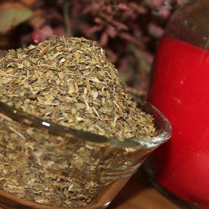 May include: A glass bowl filled with dried green herbs. The bowl is sitting on a wooden surface next to a red candle in a glass jar.