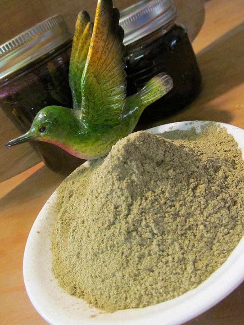 Puede incluir: Un taz&oacute;n blanco lleno de una gran cantidad de polvo verde claro. Una figurita de colibr&iacute; verde y amarillo est&aacute; posada en el borde del taz&oacute;n.