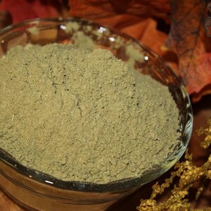 May include: A glass bowl filled with a light green powder. The powder is finely ground and has a uniform texture.