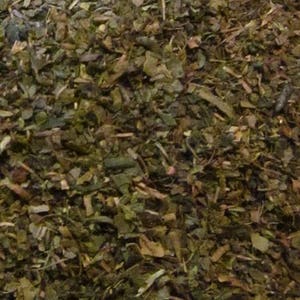 May include: Close-up of a pile of loose leaf green tea. The tea leaves are a mix of dark green and brown, with some small pieces of stem.