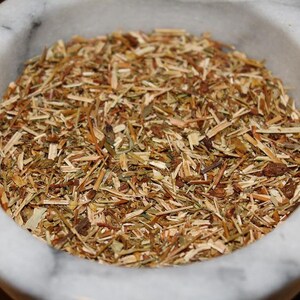 May include: A white ceramic bowl filled with dried herbs, including brown, green, and yellow pieces.