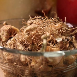 May include: A glass bowl filled with dried, light brown, fibrous roots and pieces of dried fruit.