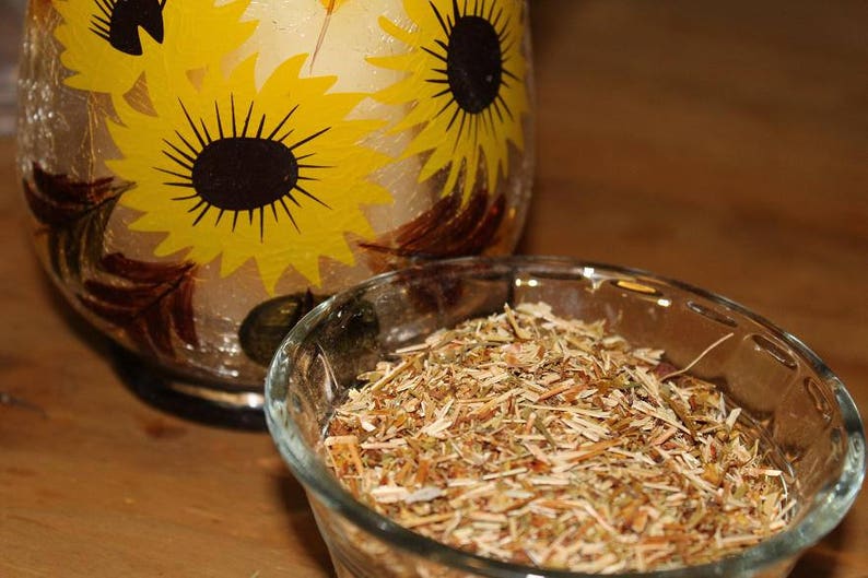 May include: A clear glass bowl filled with dried herbs, sitting on a wooden surface. The bowl is next to a glass vase with a sunflower design.