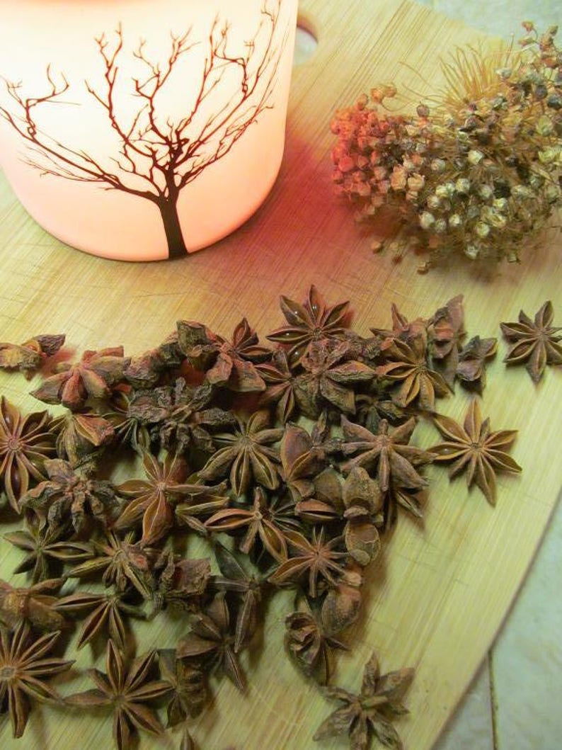 May include: A close-up of a pile of star anise pods on a wooden surface. The pods are brown and have a star shape. There is a candle holder with a tree design in the background.