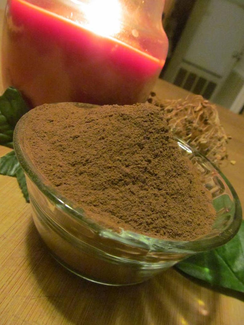 May include: A glass bowl filled with a heaping amount of dark brown powder. The powder is finely ground and has a smooth, even texture. The bowl is sitting on a wooden surface.