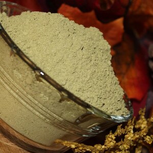 May include: A glass bowl filled with a light green powder. The bowl is sitting on a wooden surface with a brown and gold background.