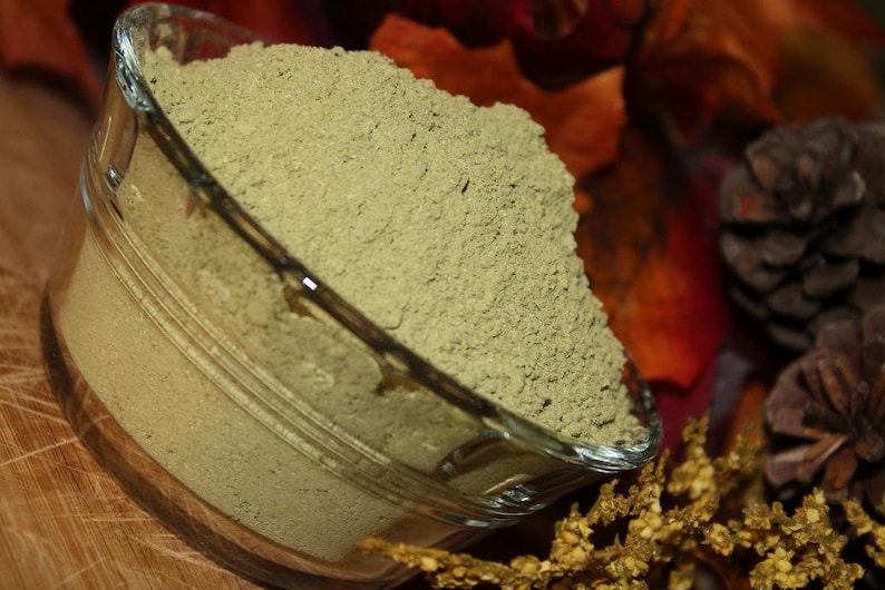 May include: A glass bowl filled with a light green powder. The bowl is sitting on a wooden surface with a brown and gold background.