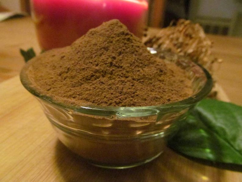 May include: A glass bowl filled with a heaping amount of brown powder, likely cocoa powder or a similar spice. The bowl is sitting on a wooden surface.