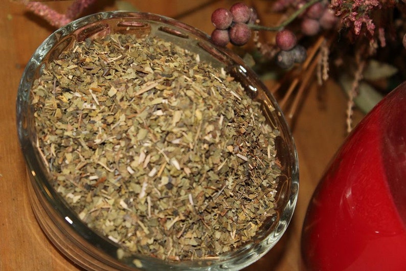 May include: A glass bowl filled with dried green herbs, likely for tea or cooking. The bowl is on a wooden surface.