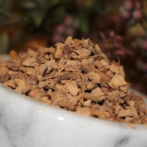 May include: A white marble mortar and pestle filled with dried, brown, and slightly reddish-brown pieces of ginger root.