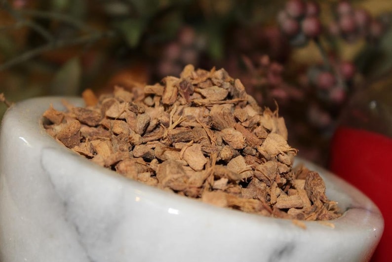May include: A white marble mortar and pestle filled with dried, brown, and slightly reddish-brown pieces of ginger root.