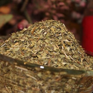 May include: A glass bowl filled with dried green herbs. The herbs are loose and appear to be a blend of different types.