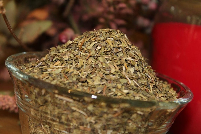 May include: A glass bowl filled with dried green herbs. The herbs are loose and appear to be a blend of different types.