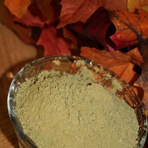 May include: A glass bowl filled with a light green powder, sitting on a wooden surface with fall leaves in the background.