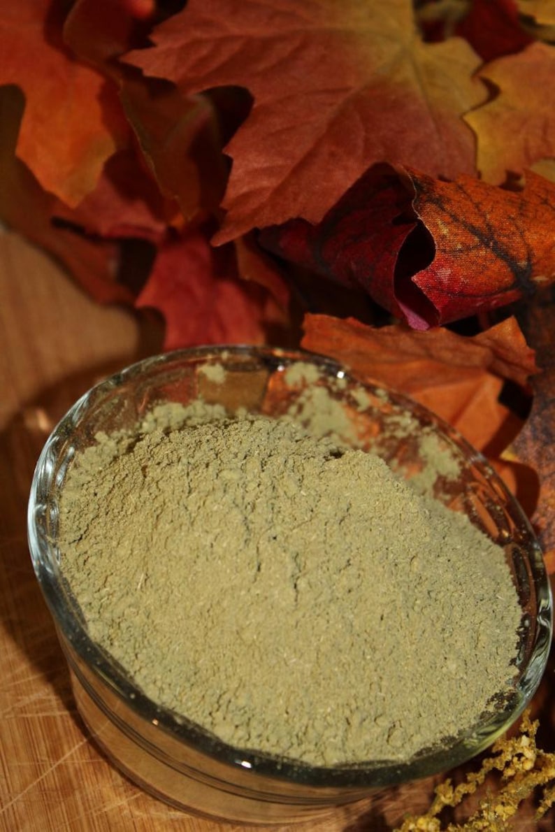 May include: A glass bowl filled with a light green powder, sitting on a wooden surface with fall leaves in the background.