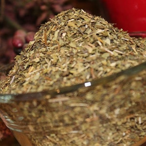 May include: A glass bowl filled with dried green herbs. The herbs are loose and appear to be chopped or shredded.