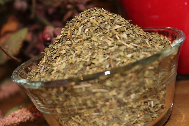 May include: A glass bowl filled with dried green herbs. The herbs are loose and appear to be chopped or shredded.