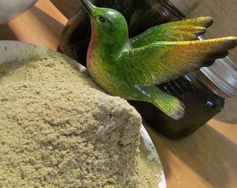 May include: A white bowl filled with a large mound of light green powder. A green and yellow hummingbird figurine is perched on the edge of the bowl.