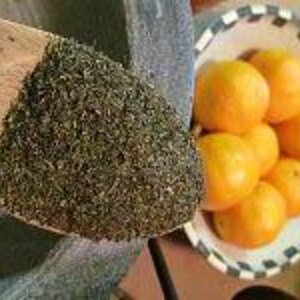 May include: A wooden spoon filled with loose green tea leaves. A bowl of five whole oranges sits next to the spoon.