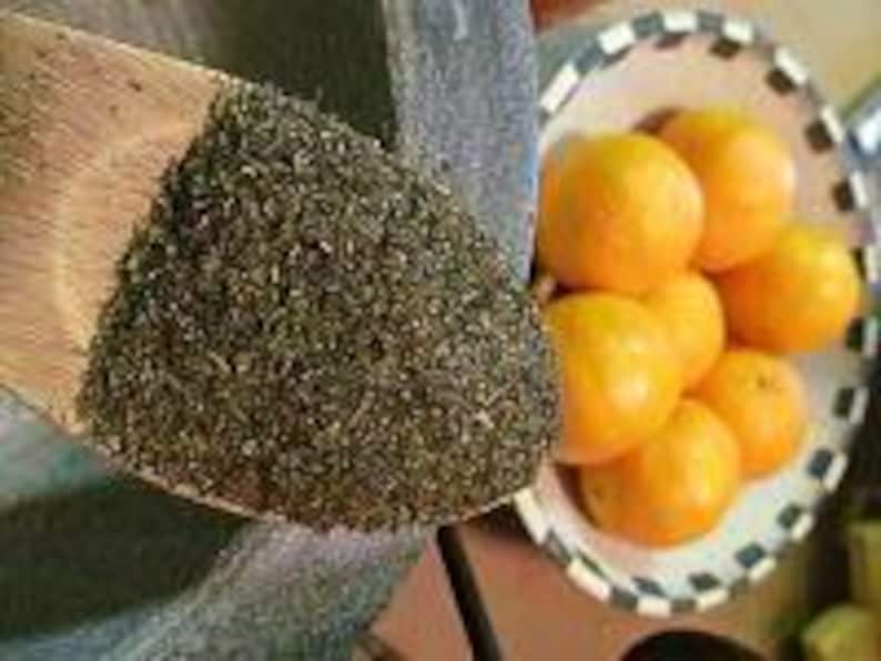 May include: A wooden spoon filled with loose green tea leaves. A bowl of five whole oranges sits next to the spoon.