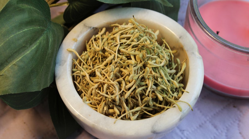 May include: A white marble bowl filled with dried, light brown flower buds. The bowl is sitting on a white surface.