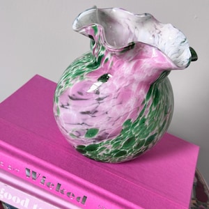 May include: A hand-blown glass vase with a ruffled, flared rim. The body features a marbled pattern of white, soft pink, and deep forest green glass. The vase has a rounded, bulbous shape and a smooth, glossy finish throughout the entire piece.