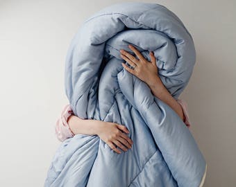 May include: A person is wrapped in a light blue comforter with a white trim. The comforter is quilted with a diamond pattern.