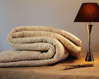 May include: A folded ivory-colored comforter or duvet sits on a brown linen surface. A gold table lamp with a dark brown lampshade is in the background.