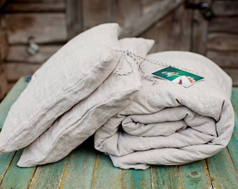 May include: A set of two linen pillowcases and a linen duvet cover in a light beige color. The duvet cover is rolled up and the pillowcases are stacked on top of it. The set is sitting on a green wooden surface.