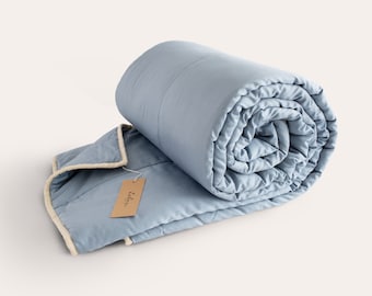 May include: A light blue weighted blanket rolled up with a beige tag that says "Lila" on it.