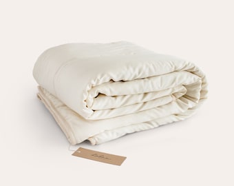 May include: A white, organic cotton quilt folded neatly with a brown tag that reads "lahora" on it.