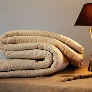 May include: A folded cream-coloured duvet or comforter on a brown surface with a silver table lamp with a black lampshade in the background.