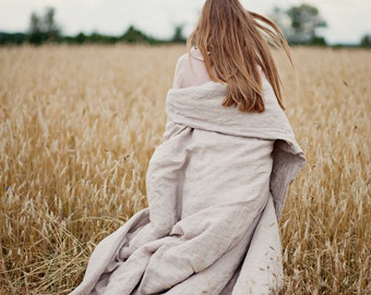 May include: A woman walks through a field of tall, dry grass, wearing a light pink shirt and a long, flowing linen blanket.